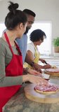 Vertical video of smiling diverse female and male friends making pizza in kitchen, in slow motion. Cooking, friendship and lifestyle concept.