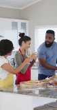 Vertical video of happy, diverse female and male friends making pizza, drinking wine, slow motion. Cooking, friendship and lifestyle concept.