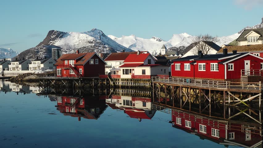 Reflection in the water. Snowy mountains, fishing village, red rorbu houses, and their peaceful reflections on the water. Breathtaking landscape of Lofoten islands, Norway. View of fjord, reflection.