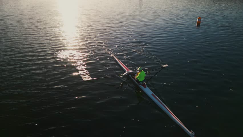 Aerial view of young woman single rower at sunrise. Young solo rower rows through a calm ocean bay at sunrise in Halifax, Canada. Caucasian woman training a rowing boat  Royalty-Free Stock Footage #3461084291
