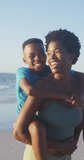 Vertical video of happy african american mother and son having fun on beach. Holidays, vacations, summer, family and relationship concept.