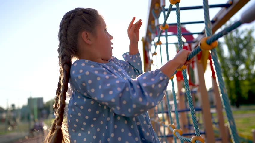 child plays on the playground. concept of happy childhood and loving family. a child smiles joyfully and climbs a ladder on a playground, the glare lifestyle of the sun in the background