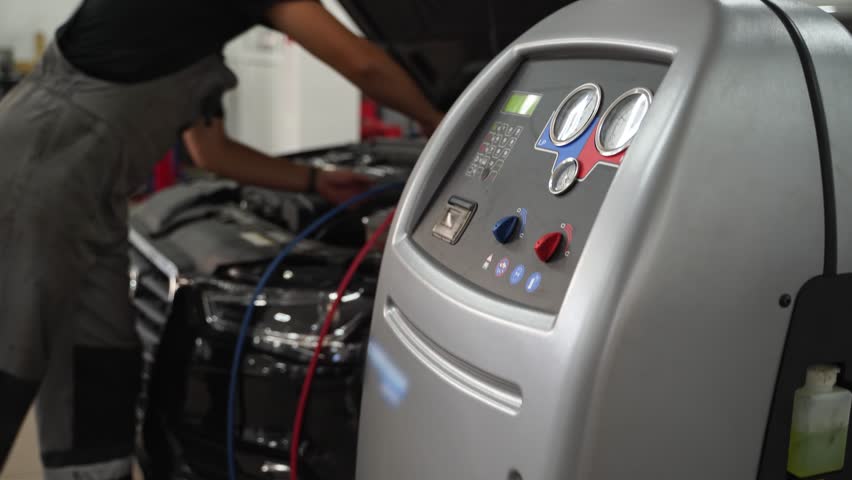 Auto mechanic refills refrigerant in car AC system. Service station equipment recharges air conditioner. Technician operates AC servicing machine, vehicle maintenance, coolant top-up procedure.