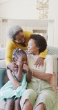 Vertical video of african american mother, daughter and grandmother embracing at home, slow motion. Happiness, family, togetherness and domestic life concept.