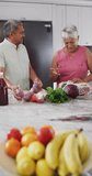 Vertical video of happy senior biracial couple talking and holding vegetables. Spending quality time at home, retirement and lifestyle concept.