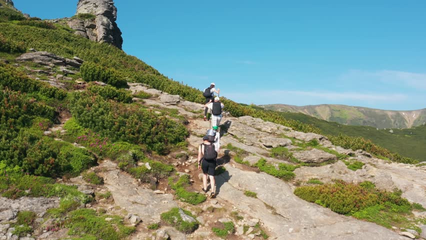 Tourists climb to the top of the mountain on rocky slopes, a beautiful view. Hike in the mountains of the tourist group, green area