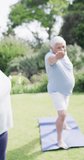 Vertical video of happy senior biracial woman doing yoga with friends in garden, in slow motion. Healthy, active senior lifestyle.