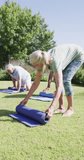 Vertical video of happy diverse senior men and women rolling up yoga mats in garden, in slow motion. Healthy, active senior lifestyle.