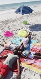 Vertical video of happy african american family having fun on beach, lying on sand. Holidays, vacations and spending quality family time together concept.