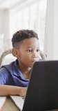 Vertical video of happy african american boy using laptop for online lesson, in slow motion. Spending quality time, domestic life and childhood concept.
