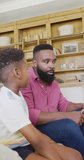 Vertical video of african american father and son sitting on sofa and talking, in slow motion. Spending quality time, domestic life and childhood concept.