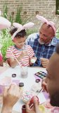 Vertical video of african american grandfather and grandson painting eggs for easter, slow motion. Easter, celebration, family, childhood and tradition concept.