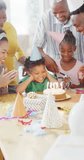 Vertical video of african american family birthday, son blowing out candles on cake, slow motion. Family, celebration and togetherness concept.