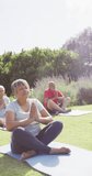 Vertical video of happy senior biracial woman doing meditation with friends in garden, slow motion. Healthy, active senior lifestyle.