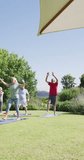Vertical video of happy diverse senior men and women doing yoga in sunny garden, in slow motion. Healthy, active senior lifestyle.