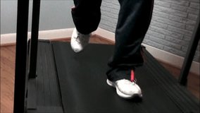 A close-up video of a mans feet, walking on a treadmill.