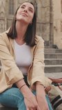 Vertical video, Happy girl traveler resting while sitting on the steps of an old building in the historic part of an old European city, camera is moving closer
