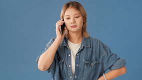 Young woman dressed in denim shirt talking on mobile phone with an angry, upset or serious face isolated on blue background in studio - Powered by Shutterstock - Get 15% off with code: PIKWIZARD15