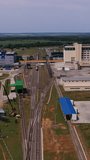 Railways with cargo trains crossing the industrial plant area. Elevator plant premises and silo containers on both sides of railways. Aerial view. Vertical video