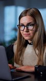 Young business lady sitting at the desk and printing something at laptop. Woman is smiling and nodding her head approvingly. Blurred background. Vertical video