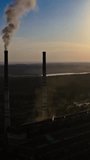 Dark silhouette of a factory at sunset. Manufacture releases harmful smoke into the air. Nature in danger. Industrial plant near the river in the evening. Vertical video