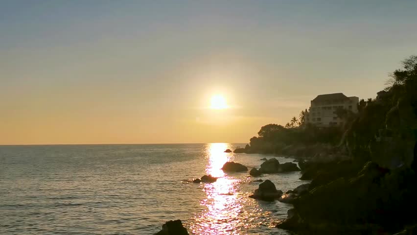 Beautiful stunning colorful and golden sunset in yellow orange red on beach and big huge surfer wave and rocks cliff panorama in tropical nature in Zicatela Puerto Escondido Oaxaca Mexico.