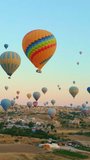 Vertical video. In this aerial video, the skies above Cappadocia, Turkey, come alive with a kaleidoscope of hot air balloons. Against the backdrop of the region's iconic valleys, rocks, and fields