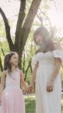 Mom, daughter are walking in park, weekend. Mother holding her daughter's hand in park. Happy family concept. Vertical video