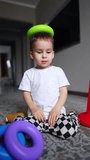 Adorable Caucasian baby sits on the floor with a pyramid detail on his head. Low angle view on the child playing at home. Vertical video.