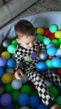 Happy cheerful kid in checkered pajama sits in the dry pool. Energetic toddler having fun time at home. Top view. Vertical video.