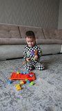 Lovely baby boy wearing black and white pajama plays on the floor with a toy. Cute child having fun at home. Vertical video.