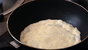A man turns over a pancake being cooked in a frying pan. Cooking food, close-up.