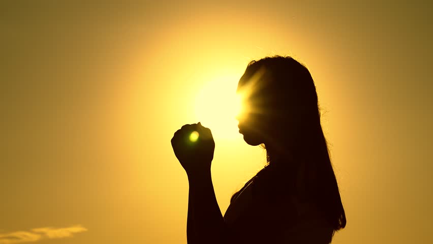 Relaxation and meditation in nature. Silhouette. Faith in god. Christian woman praying at sunset close-up. Girl on background of sky in rays of sun prayer to family and children. Apologize. Hope. Sky