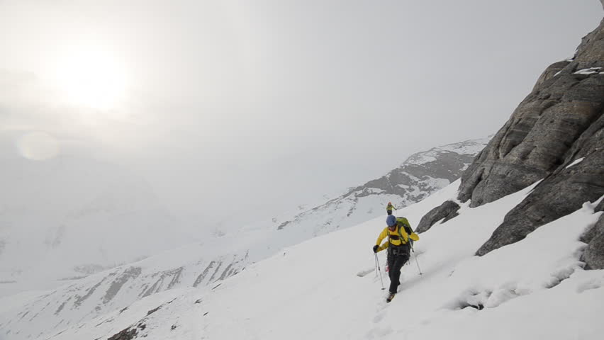 A group of mountain climbers with backpacks full of gear hike along a snow covered mountain side in the Alaskan wilderness