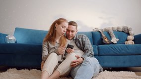 Boyfriend and Girlfriend Shopping on Internet, Couple Use Smartphone Device, while Sitting on a Couch in Cozy Apartment. Watching Funny Videos, Use Social Media, Streaming Service. Love relationship