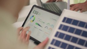Close-up of a businesswoman's hands pointing at an ESG (Environmental, Social, and Governance) report on a tablet screen, with solar panels and data charts visible. - Powered by Shutterstock - Get 15% off with code: PIKWIZARD15