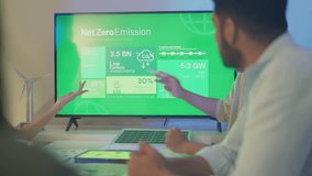 A corporate team is engaged in a strategic discussion around a large screen presenting Net Zero Emission goals, emphasizing renewable energy and sustainability targets. - Powered by Shutterstock - Get 15% off with code: PIKWIZARD15