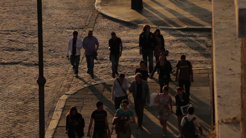 Crowds of people walk down a sidewalk at sunset