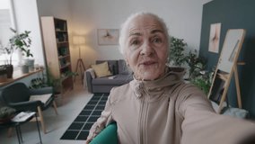 Handheld POV shot of Caucasian senior woman with rolled yoga mat under arm recording video blog during domestic sports training