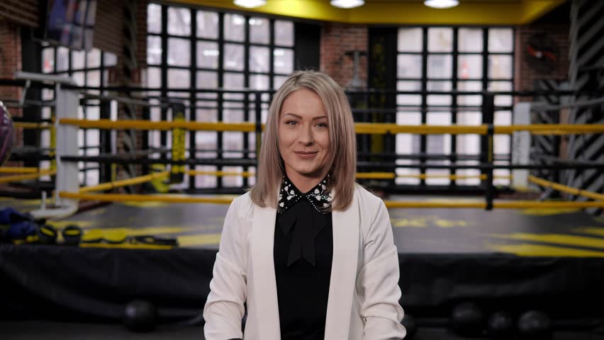 A happy businesswoman-a boxer in a white business suit and boxing gloves in the boxing ring, she raises her hands up. The concept of a successful business.