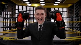 Portrait of a happy successful businessman in a black business suit and boxing gloves in a boxing ring. The concept of a successful business. - Powered by Shutterstock - Get 15% off with code: PIKWIZARD15