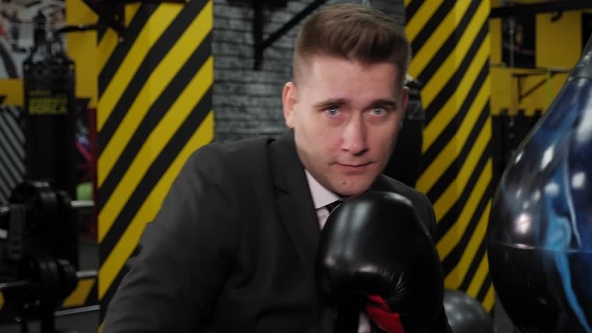Close-up of a successful happy businessman in boxing gloves, boxing in the ring after a long working day in front of the camera.