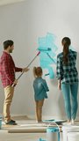 Back Shot of a Young Family Painting Walls with Their Cute Small Daughter. They Paint with Rollers that are Covered in Light Blue Paint. Room Renovations. Vertical Screen
