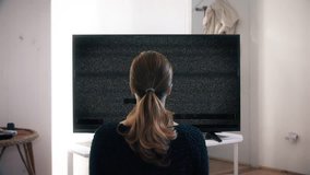Watching TV Static Noise Video Glitch. Zoom in young woman watching big screen television at home. Shot behind model shoulders.
