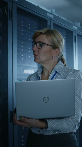 In Data Center: Female IT Technician Running Maintenance Programme on a Laptop, Controls Operational Server Rack Optimal Functioning. Modern Supercomputer. Vertical Screen Orientation Video 9:16 Royalty-Free Stock Footage #3462158549