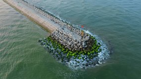 Sea breakwater with tetrapod concrete pillars covered with green moss with ocean waves, aerial footage from drone.
