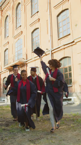 Vertical tracking shot of multicultural cheerful students throwing their hats up while celebrating graduation on-campus Royalty-Free Stock Footage #3462184377