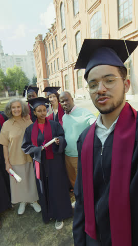 POV shot of student in hat and gown taking selfie with his collegemates and parents during graduation ceremony