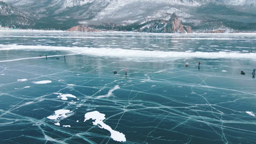 Men during hike across frozen Lake Baikal with sledges equipped with backpacks in winter. Tourists moving exploring beauty of nature with magnificent background of mountain range. Sport tourism travel