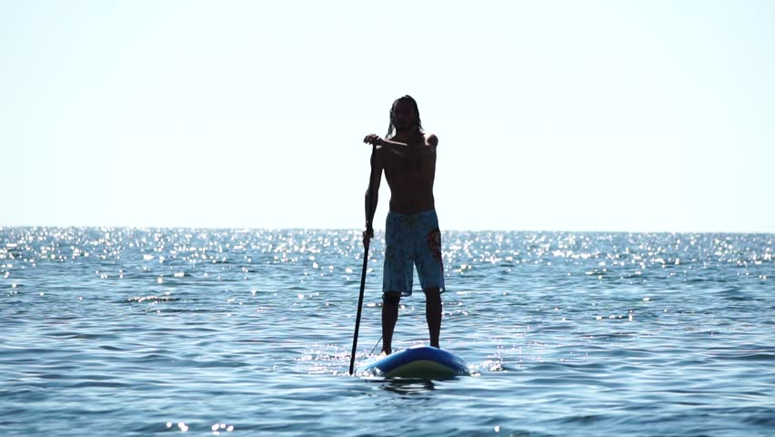 Man Sup Sea. Strong athletic man learns to paddle sup standing on board in open sea ocean on sunny day. Summer holiday vacation and travel concept. Aerial view. Slow motion